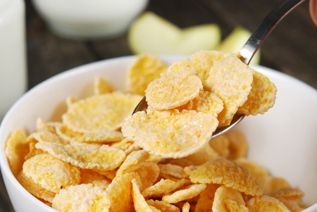 Corn flakes in small white bowls with a jar of yogurt and a spoon on a dark wooden background
