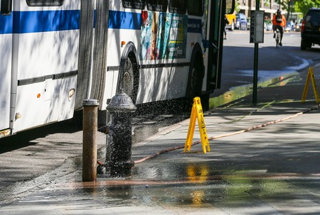 A bus stops in front of an open fire hydrantのeditorial素材