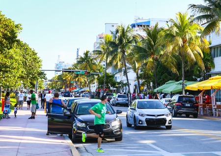 Cars driving and parking in Miami Beach on Ocean Drive, people walking by or running.のeditorial素材