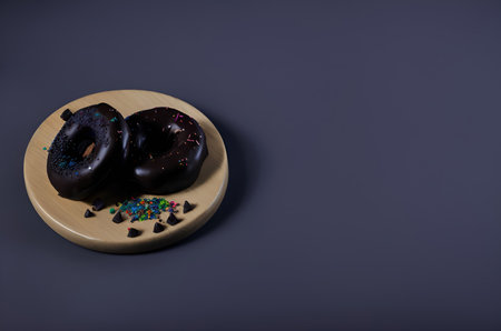 Chocolate donuts with sprinkles on wooden plate on dark backgroundの写真素材