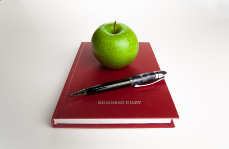 open diary with large pen and green apple on whiteの写真素材