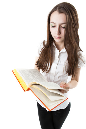 young girl is reading a book while standing isolated on a white backgroundの写真素材