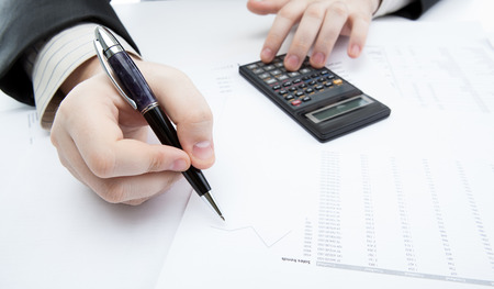 businessman holding a pen and counts the budget on the desktopの写真素材