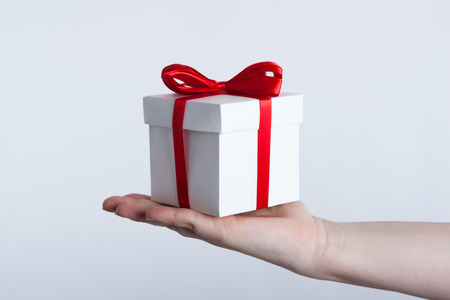 white gift box with red ribbon in hand on grey backgroundの写真素材