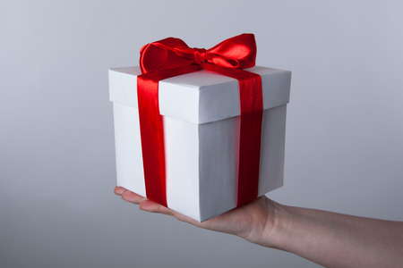 white gift box with red ribbon in hand on grey backgroundの写真素材