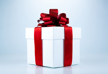 White gift box with red ribbon and bow on grey backgroundの写真素材