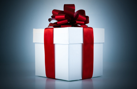 White gift box with red ribbon and bow on blue backgroundの写真素材