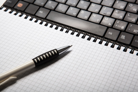 pen on a notebook into a cell and keyboard close upの写真素材