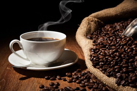 cup of coffee, coffee beans and bag on a wood tableの写真素材