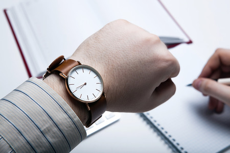 Workplace businessman looks at the clock and office toolsの写真素材