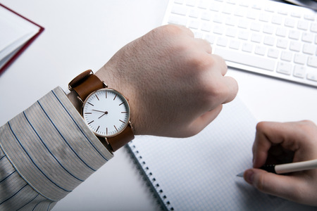 Workplace businessman looks at the clock and office toolsの写真素材
