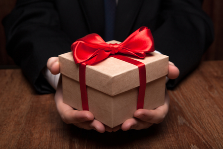 white gift box with red ribbon in hand close upの写真素材