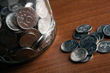 bank with coins and a bunch of Russian rubles coins on a wooden surface close upの写真素材