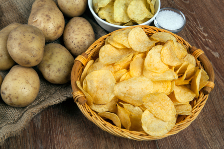 still life from a basket with potato chips and raw potatoes on a wooden tableの写真素材