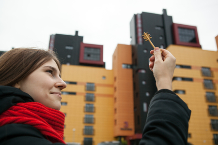 a girl holds the keys to the apartment on the background of new buildingsの写真素材
