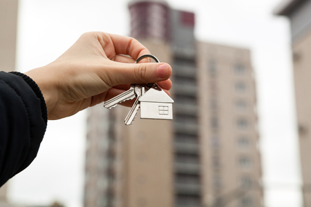 A woman's hand holds the keys on the background of new buildingsの写真素材