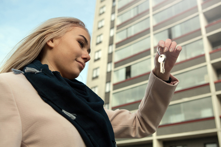 a girl holds the keys to the apartment on the background of new buildingsの写真素材