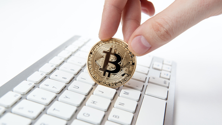 hand holds a golden coin of bitcoin above the keyboardの写真素材