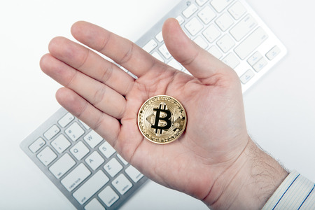 hand holds a golden coin of bitcoin above the keyboardの写真素材