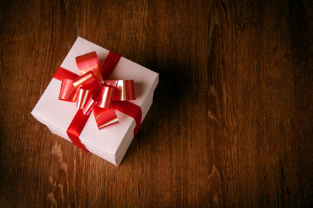 One white festive gift box with a red bow on a wooden tableの写真素材
