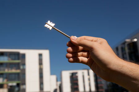 A man's hand holds the keys on the background of new buildingsの写真素材