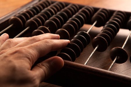 big antique abacus on a wooden table and the hand of man close upの写真素材