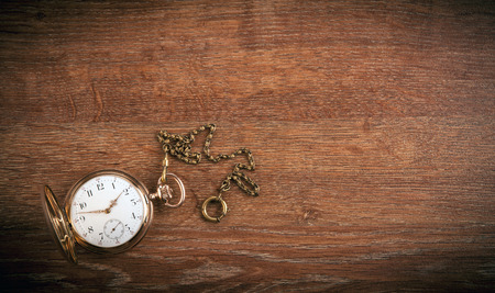 An antique gold pocket watch lies on a wooden table top viewの写真素材