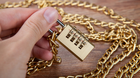 brass padlocks with a gold chain in the hand of man close upの写真素材