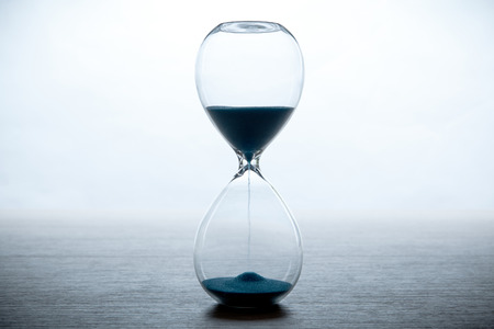 hourglass with blue sand on a white background and a gray table close up
