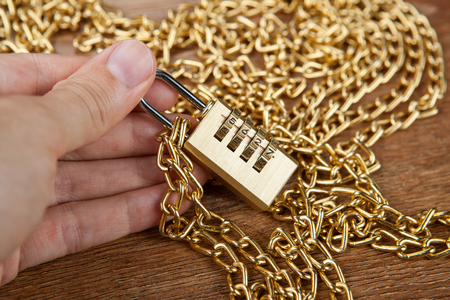 brass padlocks with a gold chain in the hand of man close upの写真素材