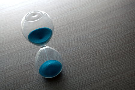 hourglass with blue sand on a gray table close upの写真素材