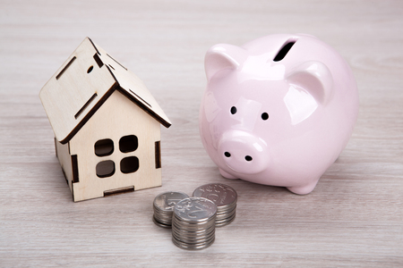 wooden miniature house and pink piggy bank with Russian ruble coins close upの写真素材