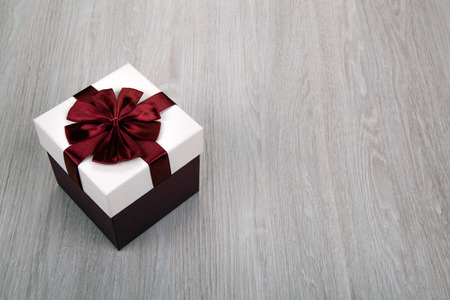 white gift box with a bow on a gray wooden background close up