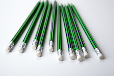 many simple pencils with erasers with green skin in a row on a white table close upの写真素材