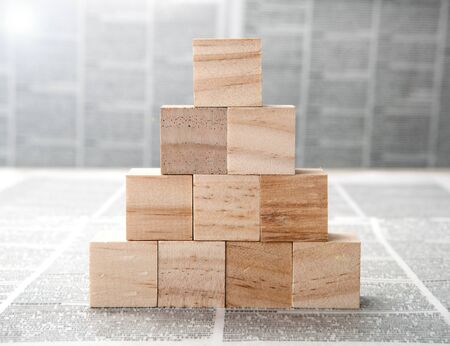 Square wooden blocks in the shape of a pyramid on a newspaper background closeupの写真素材