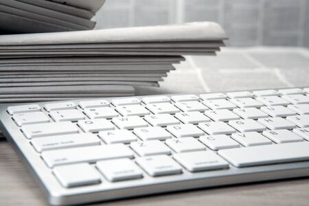 keyboard pc and piles of numerous printed newspapers closeupの写真素材