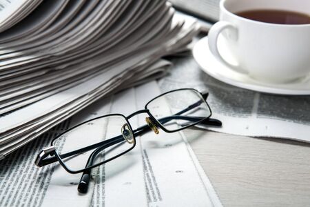 glasses on newspapers and a cup of coffee on the table closeupの写真素材