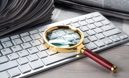 magnifier on the keyboard and a stack of newspapersの写真素材