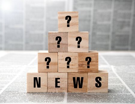News title and question marks on square wooden blocks on a newspaper background closeupの写真素材