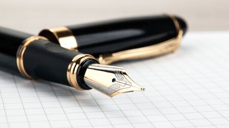 golden fountain pen on the notepad on a table closeup