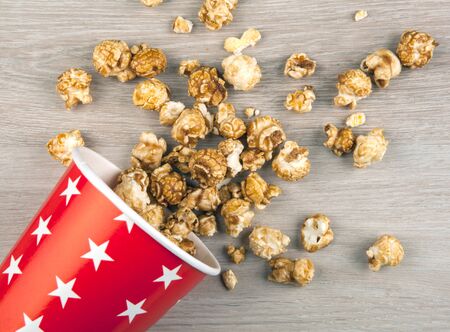 red cardboard cup with sprinkled sugar popcorn on a wooden table top viewの写真素材