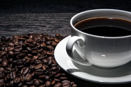 cup of hot coffee and roasted coffee beans on a wooden table closeupの写真素材