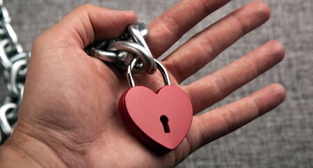 locked heart shaped padlock with steel chain in the male palmの写真素材