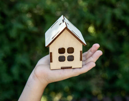 girlish children's palm is holding a miniature wooden house closeupの写真素材