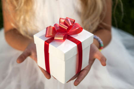 white gift box in the palms of a little girl closeup