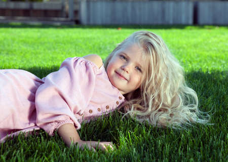 little girl in a pink dress on a green lawn portraitの写真素材