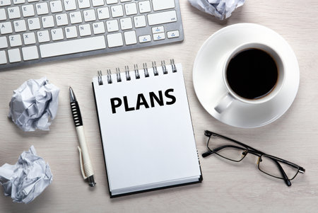 work table, a cup of coffee, a notebook with title plans with a pen and crumpled paper top viewの写真素材