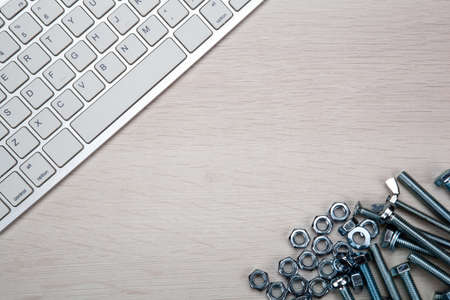 nuts screws fastening materials and pc keyboard on a wooden background top view