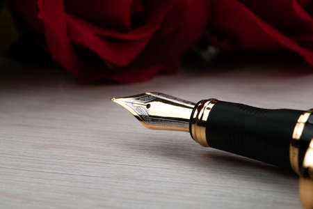 gilded pen with red roses on a wooden table closeupの写真素材