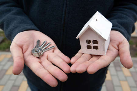 miniature wooden house and keys in handsの写真素材